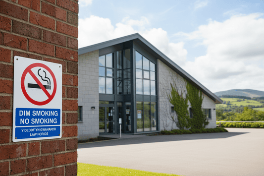 No-smoking sign mounted on the red brick wall of a school entrance, with the school building behind
