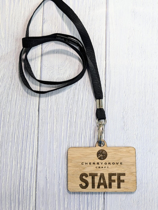 Oak staff name badge engraved with STAFF, hanging from a black breakaway lanyard