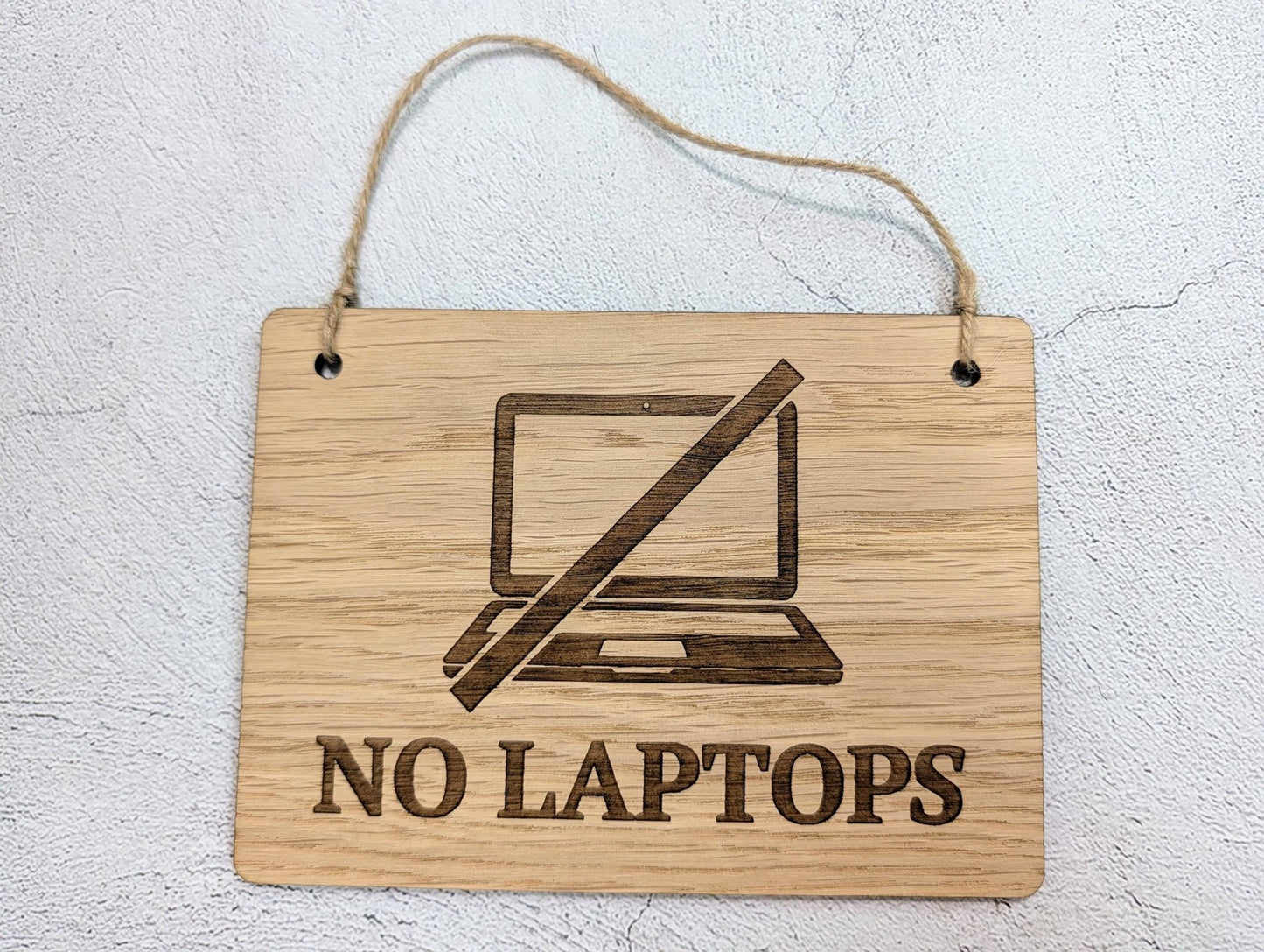 No laptops sign close-up — laser-engraved text and jute string loop detail