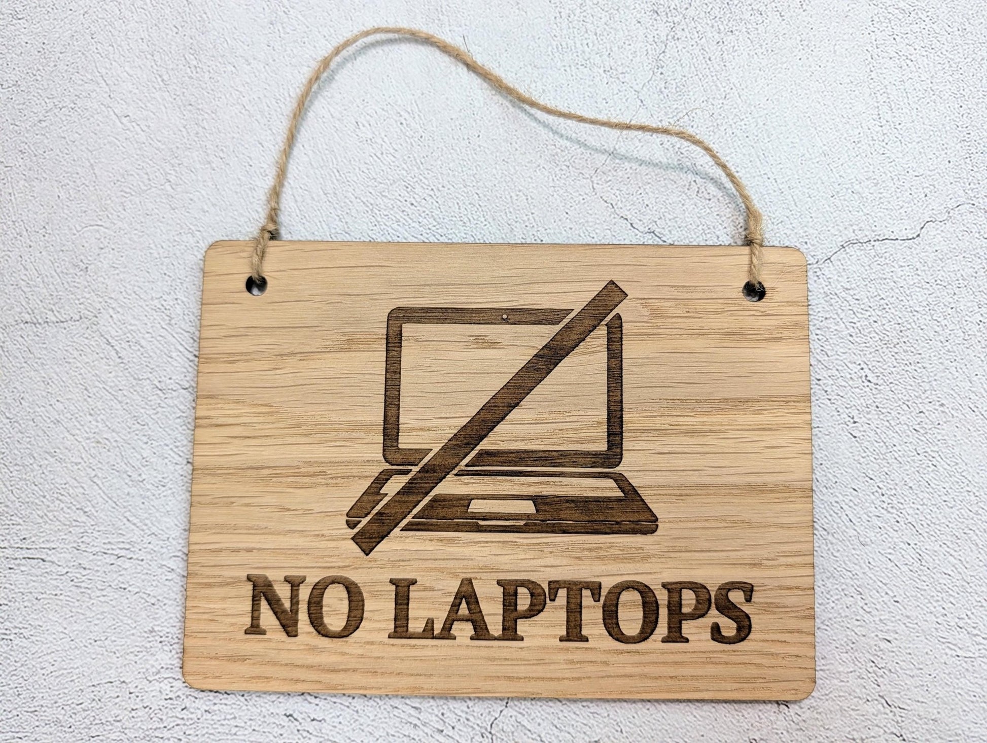 No laptops sign close-up — laser-engraved text and jute string loop detail