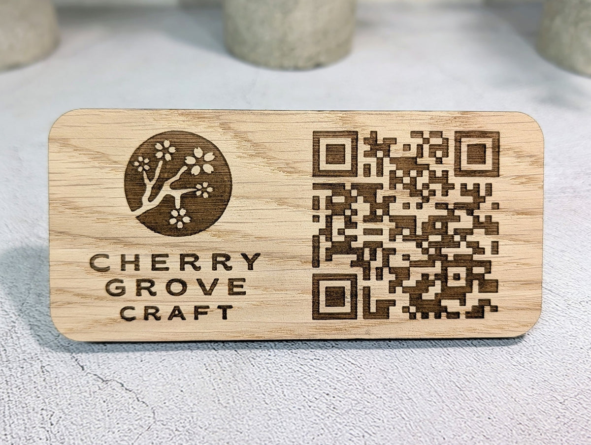 Front of the oak QR code stand, 150 × 70mm, engraved with the Cherry Grove Craft cherry blossom logo and a QR code