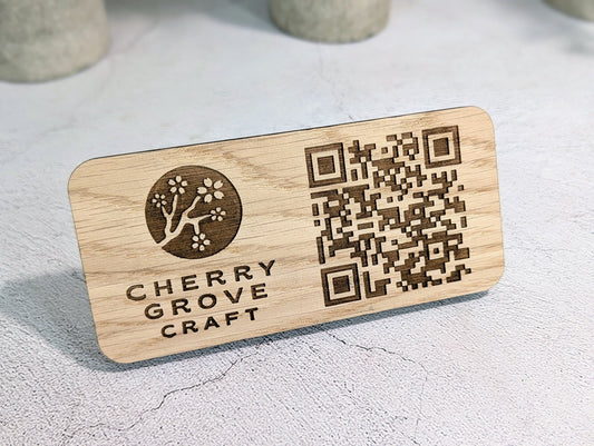 Oak QR code stand seen at an angle, showing the laser-engraved logo and QR code on the 150 × 70mm panel