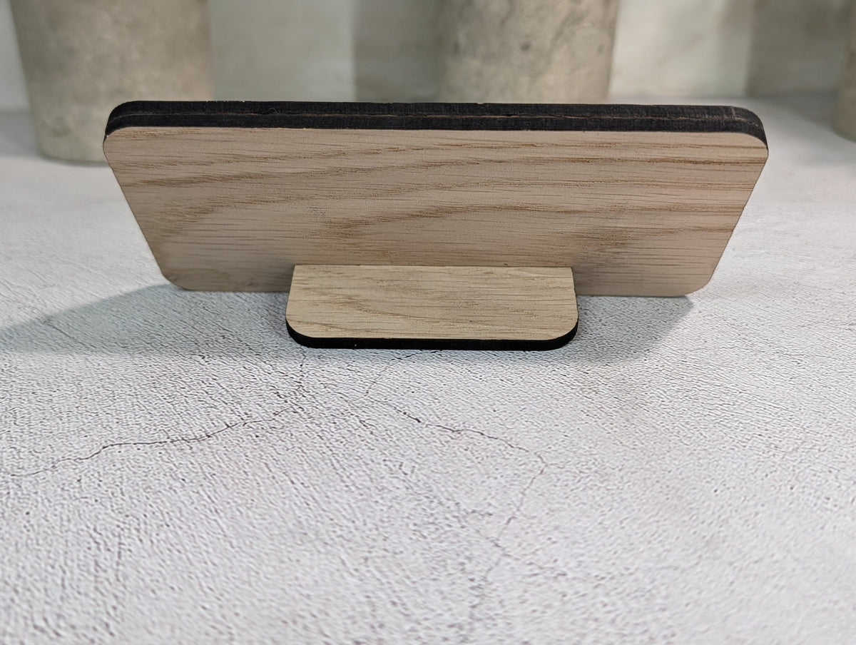 Oak QR code stand with an engraved logo and QR code standing on a table in front of potted plants